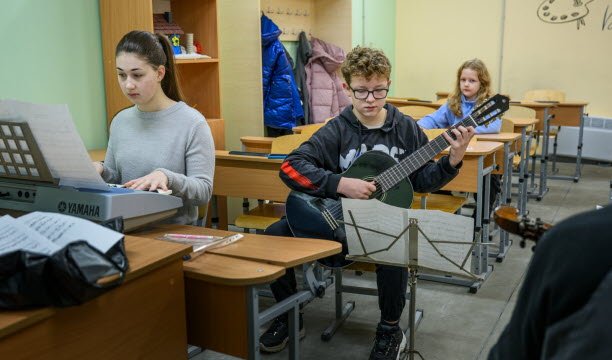 Ulliana, 10 tahun, menemani kakak laki-lakinya yang mengikuti pelajaran musik di sekolah underground. Foto EBRA/Élise Blanchard