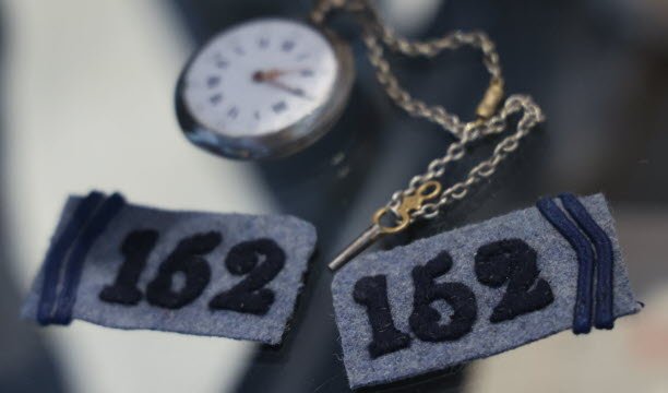 Lambang militer antik dan arloji saku awal abad ke-20 milik prajurit André Tarby, kakek buyut Camille. Jam tangan masih berfungsi dan disetel ke pukul 14.15, saat penyerangan terjadi pada tanggal 21 Desember 1915. Foto Jean-François Frey